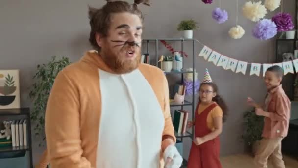 Medium shot of Caucasian male entertainer in cat costume and makeup and group of diverse preteen kids walking around in circle at birthday party, playing train game and singing fun song - Footage, Video