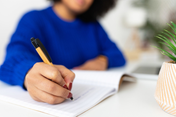 Evde dizüstü bilgisayar kullanırken not defterine not alan genç bir kadının yakın plan görüntüsü. Eline odaklan. İş ve eğitim kavramı. - Fotoğraf, Görsel