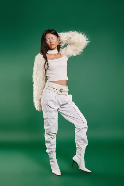 brünette asiatische Frau im total weißen Outfit und Make-up posiert auf grünem Hintergrund, Wintermode - Foto, Bild