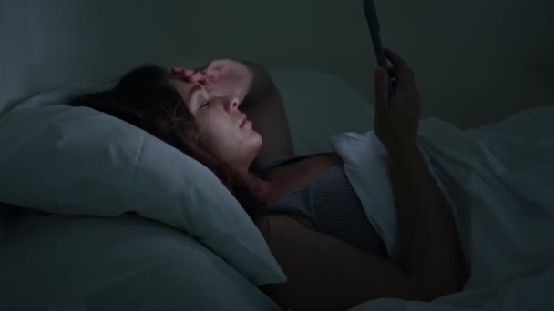 Неспокійно в ліжку, переслідування сну: молода жінка, захоплена безсонням, шукає розради в її смартфонах ніжне сяйво - Кадри, відео