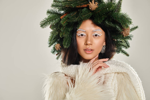 winter concept, beautiful woman with natural pine wreath posing in white clothes on grey backdrop - 写真・画像