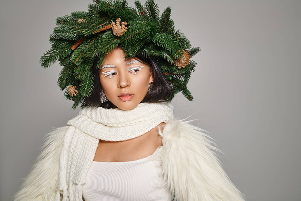 charming winter queen with white eye makeup and beads on face posing in wreath on grey background - Photo, Image