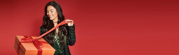 happy asian woman in green jacket with sequins pulling ribbon on gift box, Merry Christmas banner - Foto, immagini