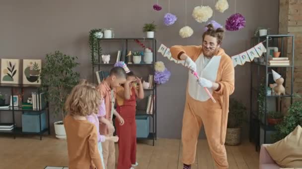 Середній повний знімок кавказького чоловічого артиста в котячому костюмі, розважаючись з різними дітьми на вечірці вдома, роблячи великі мильні бульбашки, і діти сміються, кричать і намагаються зловити їх - Кадри, відео