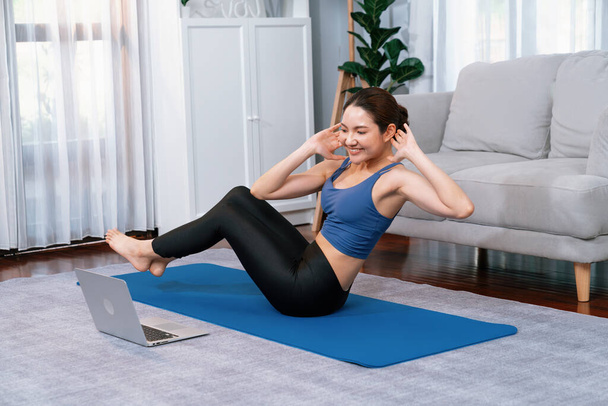 Азіатська жінка в спортивному одязі робить хрускіт на тренувальному килимку як домашнє тренування тренування рутини. Приваблива дівчина займається своїм прагненням до здорового способу життя з онлайн-тренувальним відео. Яскравий - Фото, зображення