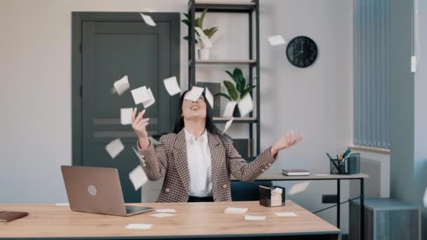 Szczęśliwa młoda kobieta biznesu świętuje sukces w biurze rzucając papier w powietrze - Materiał filmowy, wideo
