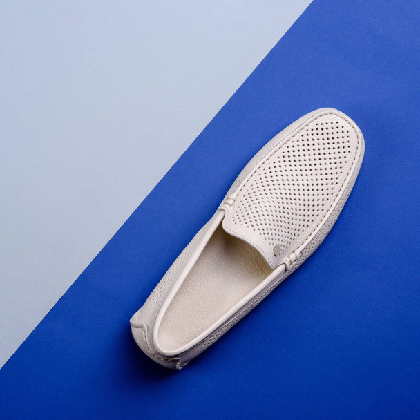 Top kilátás elegáns elefántcsont perforált bőr férfi mokaszin cipő elszigetelt kreatív kéttónusú kék háttér másolási hellyel. Kreatív minimalista elrendezés lábbelivel. Cipőbolti reklám. - Fotó, kép