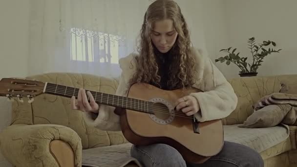 Nuori, kiharatukkainen tyttö soittaa akustista kitaraansa intohimoisesti ja lahjakkaasti kotonaan..  - Materiaali, video