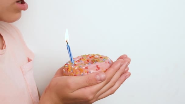 Een tienermeisje blaast een kaars uit op een roze donut. Gelukkige verjaardag of jubileum concept. Doe een wens slow motion full HD verjaardagsvideo - Video