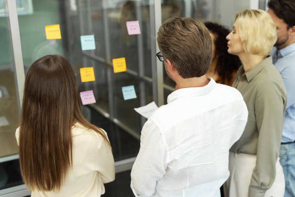 Group of businesspeople using sticky notes, agile methodology for productivity working together in modern office. Colleagues planning startup, communication at workplace. Teamwork, scrum - Photo, Image