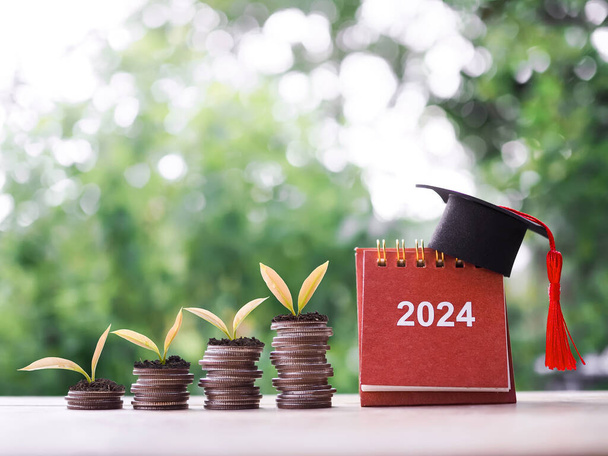 Objetivos de estudio, 2024 Calendario de escritorio con sombrero de graduación y plantas que crecen en la pila de monedas. El concepto de ahorrar dinero para la educación, préstamo estudiantil, becas, tasas de matrícula en el año nuevo 2024 - Foto, imagen