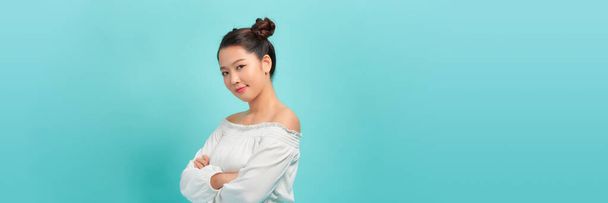 Студийный портрет милой азиатской девушки со скрещенными руками, на синем фоне. - Фото, изображение