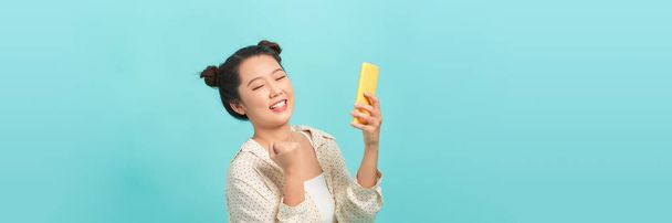 excité belle jeune asiatique femme à l'aide smartphone mobile debout sur isolé bleu fond.  - Photo, image