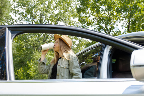 Улыбающаяся молодая женщина пьет кофе или чай из многоразового термоса. Путешественник делает перерыв на кофе в местном сольном путешествии по выходным. Вышедшая женщина исследует свободу на открытом воздухе в лесу. Единство - Фото, изображение