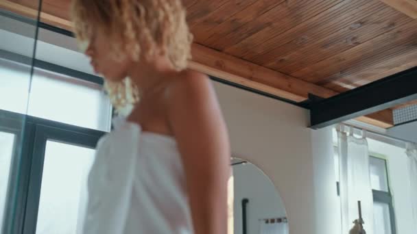 vrouw met blond krullend haar dragen witte handdoek gaat in douchecabine - Video