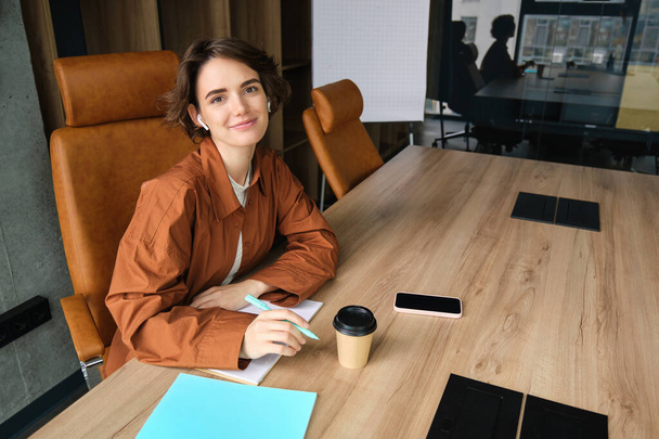 Молодая женщина работает в офисе, пьет чашку кофе в конференц-зале. - Фото, изображение