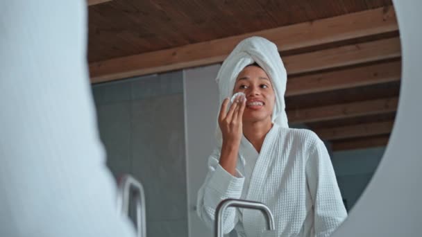 Nainen pukeutunut valkoinen kylpytakki seisoo peilin edessä hoitaa ihoa naisellinen kauneus tuotteita kylpyhuoneessa - Materiaali, video