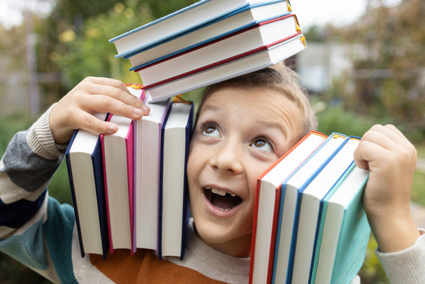 stapels boeken op de schouders van vrolijke grappige 8-jarige jongen. terug naar school. Boekendag. Lees met plezier. concept van lezen, onderwijs, wijsheid, kennis. Digitale detox. kinderfantasieën - Foto, afbeelding