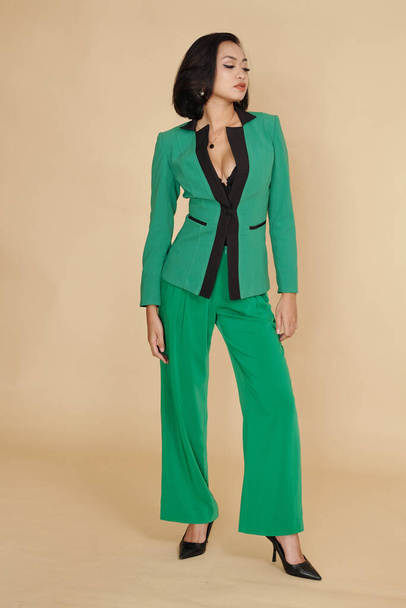 Asian fashion model demonstrating green elegant suit against beige background - Foto, afbeelding