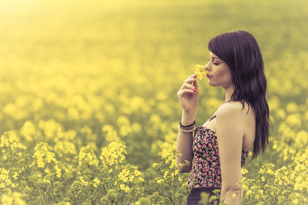 Beautiful woman in meadow of yellow flowers sniffing flower - Photo, Image