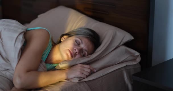 Ευτυχισμένη χαρούμενη γυναίκα ξυπνάει με τις πρώτες ακτίνες του ήλιου στο κρεβάτι. Θετική διάθεση και έννοια υγιούς ύπνου - Πλάνα, βίντεο