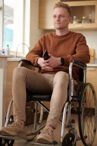 Muotokuva vakava nuori mies älypuhelin istuu pyörätuolissa ja katselee pois - Valokuva, kuva