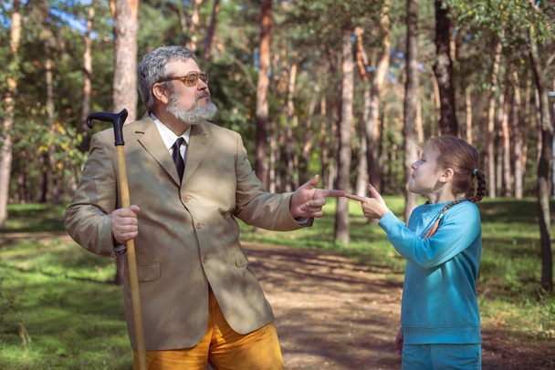 Grootvader loopt met zijn kleindochter in het park. Een grappige grootvader en een klein meisje spelen en maken grapjes.. - Foto, afbeelding