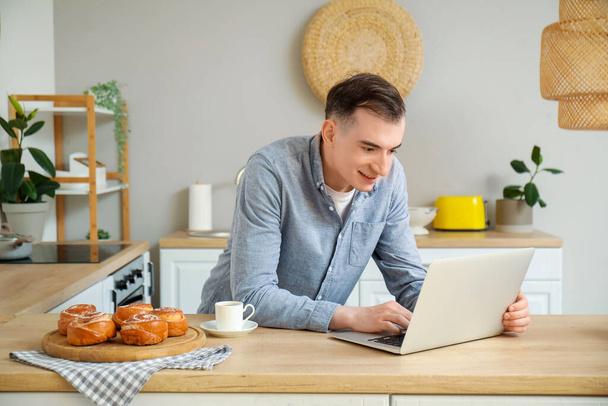 Young man with laptop messaging in kitchen - Photo, Image