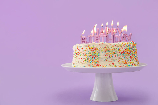 Stand avec délicieux gâteau d'anniversaire et bougies sur fond lilas - Photo, image