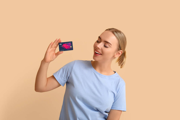 Mujer joven bonita con tarjeta de crédito sobre fondo beige - Foto, Imagen