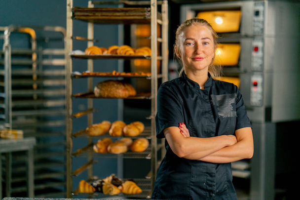 Portret van een professionele meidenbakker in een bakkerij tegen de achtergrond van ovens en een verscheidenheid aan verse gebakjes - Foto, afbeelding