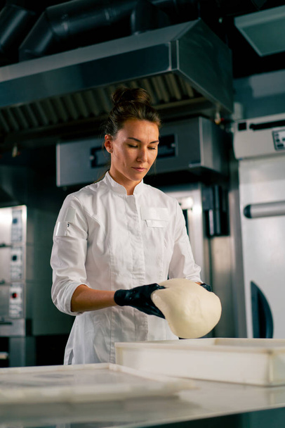 profissional padeiro feminino cuidadosamente amassa a massa para assar pão fresco em uma padaria acolhedora - Foto, Imagem