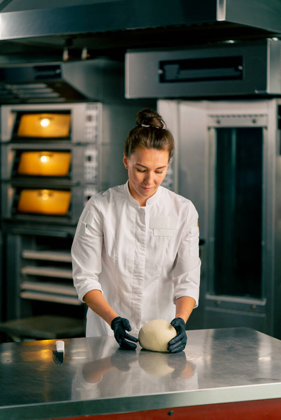 επαγγελματική γυναίκα αρτοποιός στην κουζίνα διαμορφώνει τη ζύμη σε ένα τέλειο σχήμα ψωμιού προς πώληση στο αρτοποιείο - Φωτογραφία, εικόνα