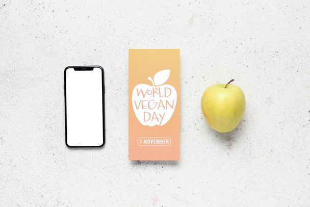 ホワイトバックグラウンドのワールド・ヴィーガン・デイ,新鮮なリンゴと携帯電話のテキスト付きカード - 写真・画像