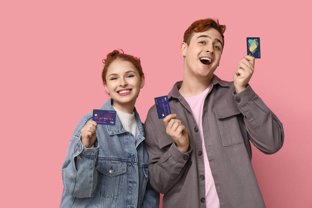 Young couple with credit cards on pink background - Photo, Image