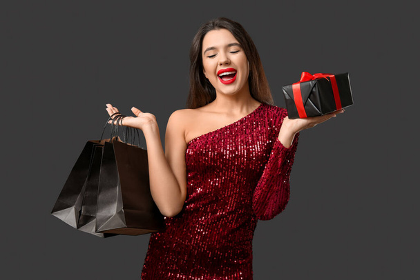 Schöne Frau mit Einkaufstaschen und Geschenkbox auf dunklem Hintergrund. Black-Friday-Verkauf - Foto, Bild