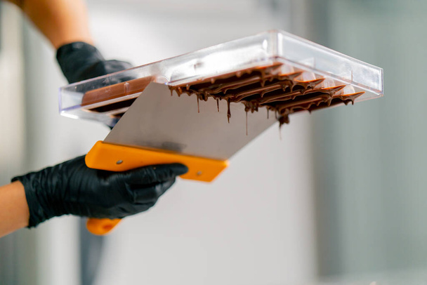 Druppels gesmolten warme chocolademelk die uit een omgekeerde vorm stroomt voor het maken van snoepjes in een snoepwinkel - Foto, afbeelding
