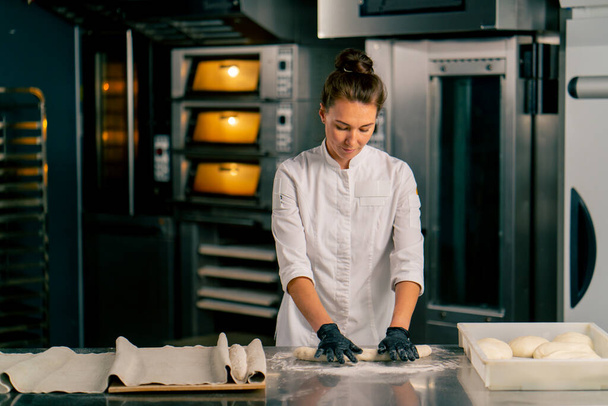 Концентрированная пекарь скручивает тесто в равные части, чтобы создать круассан перед выпечкой - Фото, изображение