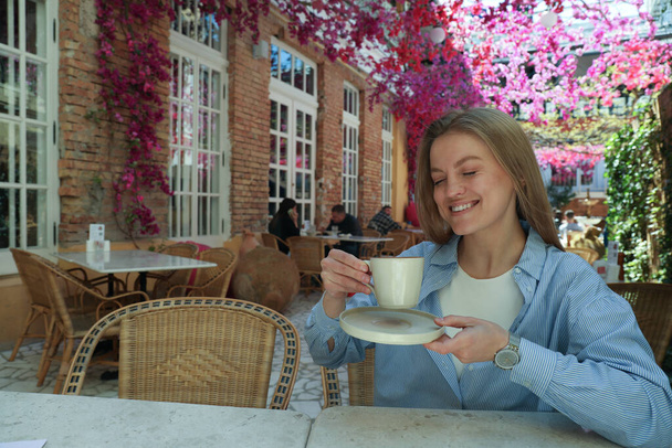 Young smiling woman with cup in hands in outdoor cafe, space for text - Photo, Image