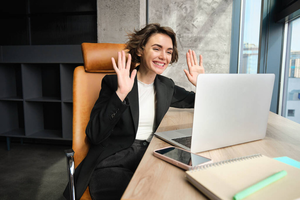 Young professional, woman connects to business meeting, online conference or chat, talking to laptop, gesturing while having conversation or giving speech. - Photo, Image