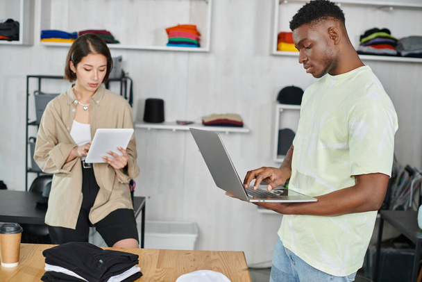 młodzi międzyrasowi przedsiębiorcy z laptopem i tabletem cyfrowym pracujący nad startem w studio druku - Zdjęcie, obraz