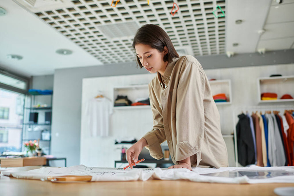 продуманий жіночий азіатський дизайнер тримає текстовий шаблон біля одягу в друкованій студії, творчість - Фото, зображення
