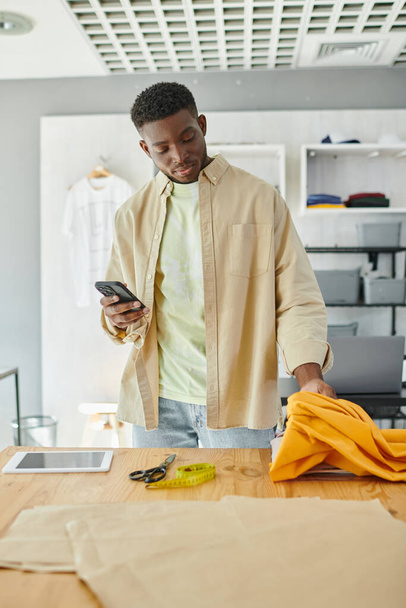 designer americano africano com smartphone tocando amostras de tecido perto de tesoura e tablet digital - Foto, Imagem