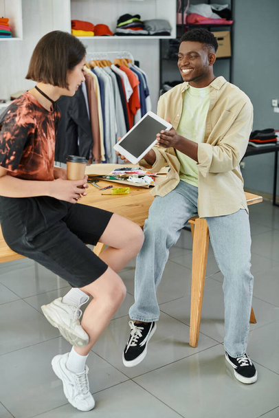 alegre africano americano diseñador mostrando digital tablet a asiático colega en textil impresión taller - Foto, Imagen