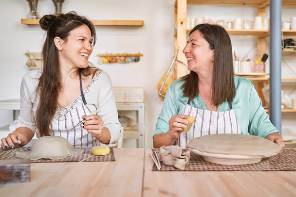Zwei Frauen in Schürzen lächeln, während sie gemeinsam in einer Keramikwerkstatt genießen. Hobby und Bastelkonzept. - Foto, Bild