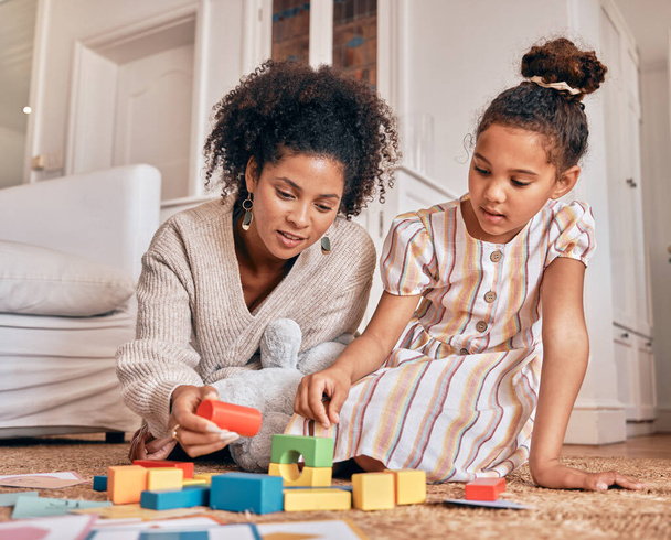 Family, education and building blocks with a daughter learning from her mother on the floor of their living room. Kids, growth and toys for child development with a woman teaching a girl at home. - Photo, Image