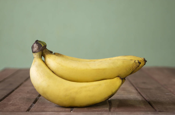 Bananenfrüchte mit Holztisch auf unscharfem grünem Hintergrund - Foto, Bild