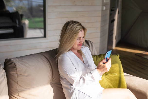 Щаслива молода біла жінка відпочиває на зручному дивані на домашньому текстовому повідомленні на смартфоні, використовує мобільний телефон, переглядає бездротовий Інтернет на гаджеті, купує онлайн з дому
. - Фото, зображення