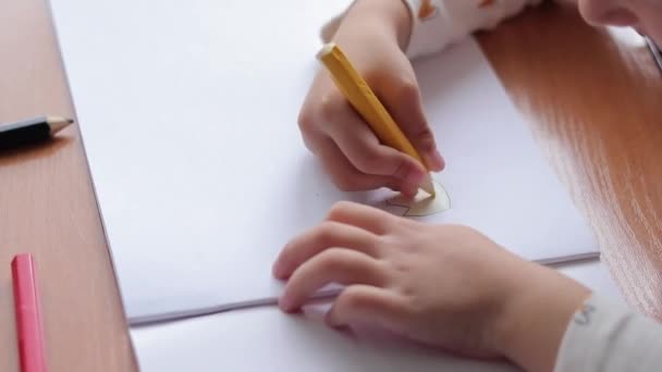 Un niño dibuja con lápices de colores en un álbum. La creatividad de los niños, el aprendizaje en el jardín de infantes, la escuela o en casa. Mano de niño con un lápiz de primer plano, enfoque selectivo. Chica dibuja un cuadro - Imágenes, Vídeo
