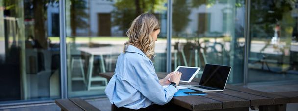 Retrato de una mujer de negocios trabajando en una tableta digital, revisando diagramas, sentada al aire libre en el aire libre cerca del edificio de oficinas. Mujer corporativa se prepara para reunión de trabajo. - Foto, Imagen
